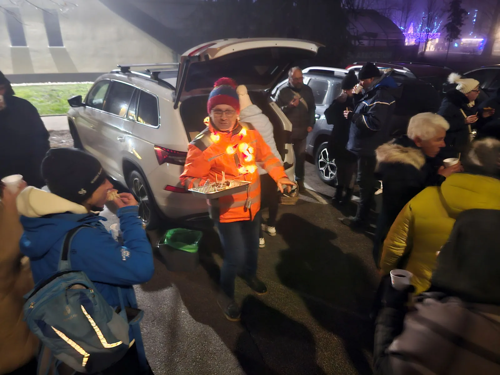 Moški v oranžnem brezrokavniku z lučkami ponuja pladenj hrane med obiskovalci