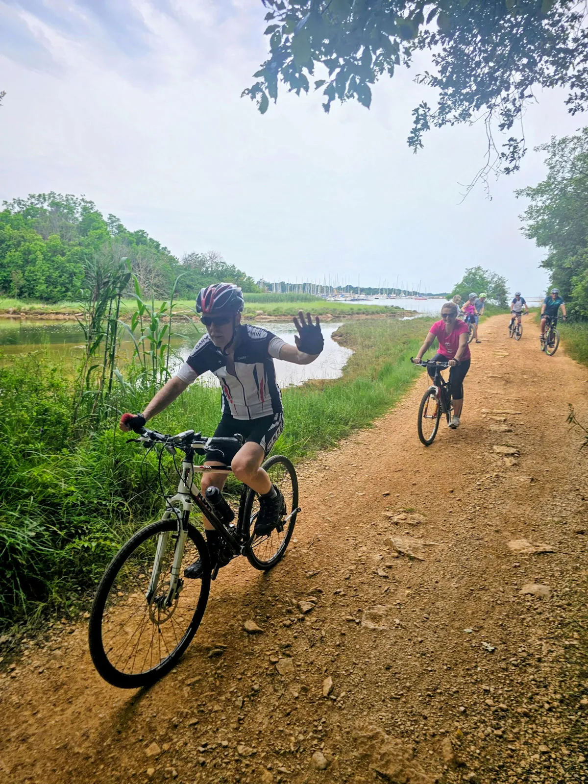 Cyclists on a gravel path by the water, one cyclist waving hello