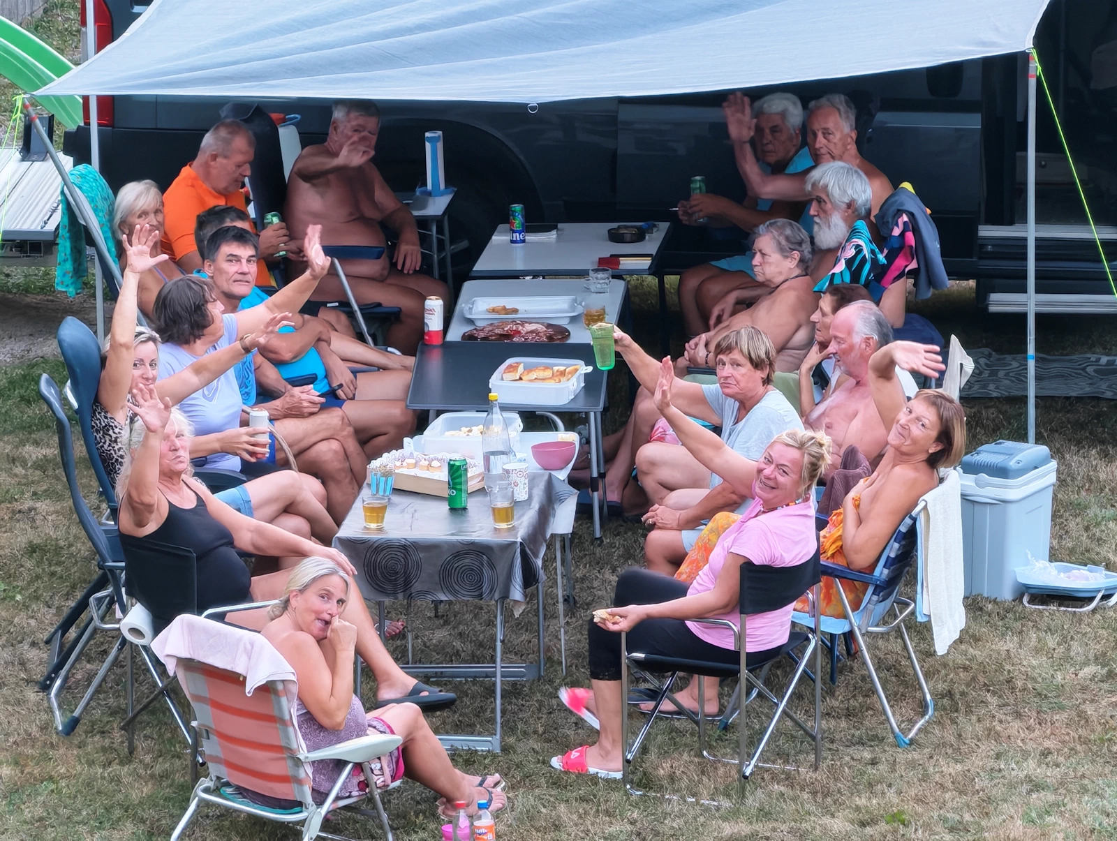 Druščina zvečer sedi za mizo pod nadstreškom ob prikolici