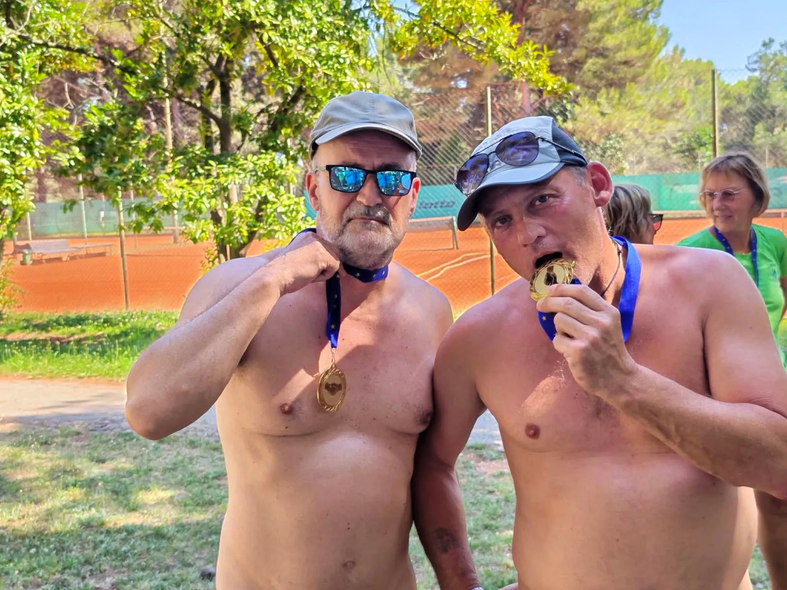Dva moška z zlatima medaljama okoli vratu na igrišču pozirata z ugrizom v medaljo