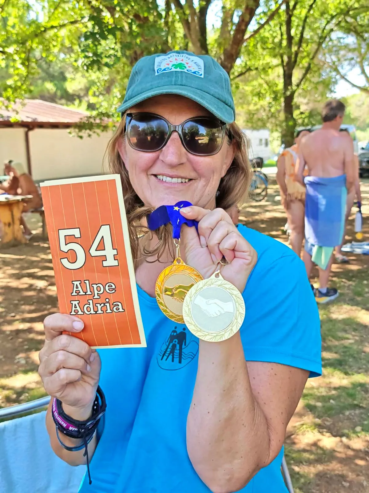 Moški v zeleni majici z medaljo hodi in v roki drži zložen list papirja