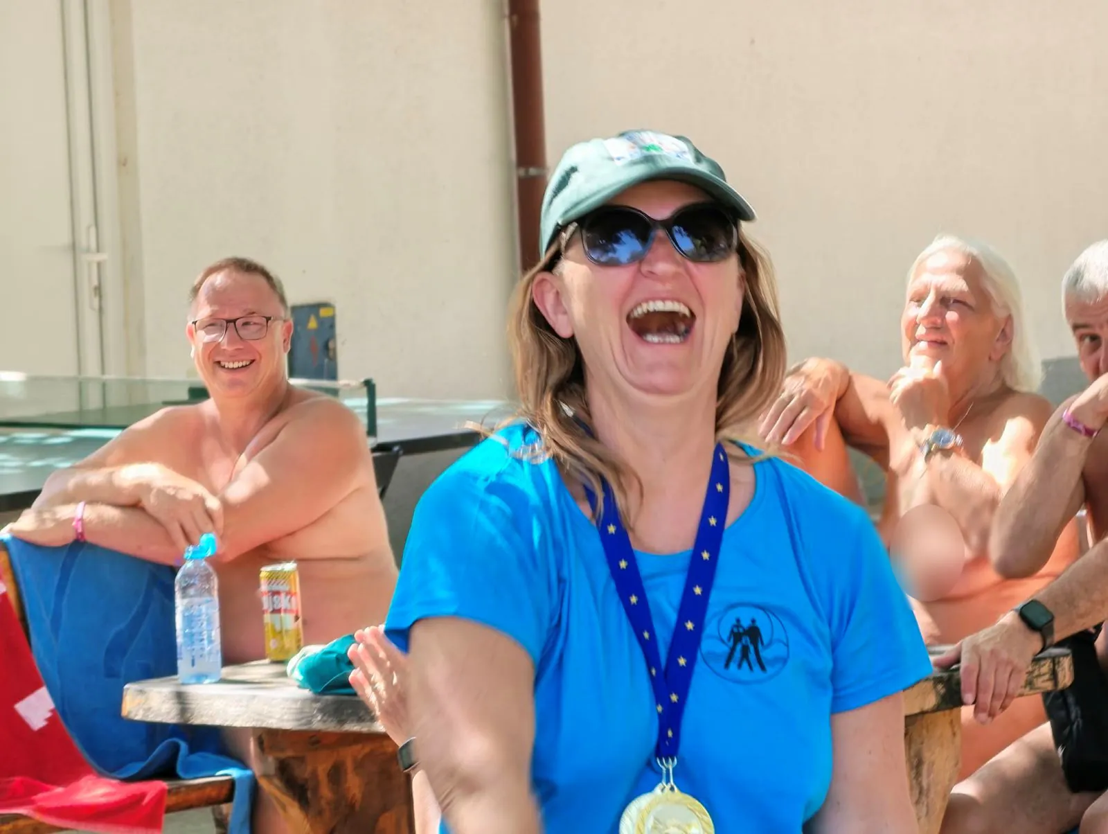 Ženska z medaljo se glasno smeje, v ozadju se smejijo tudi drugi