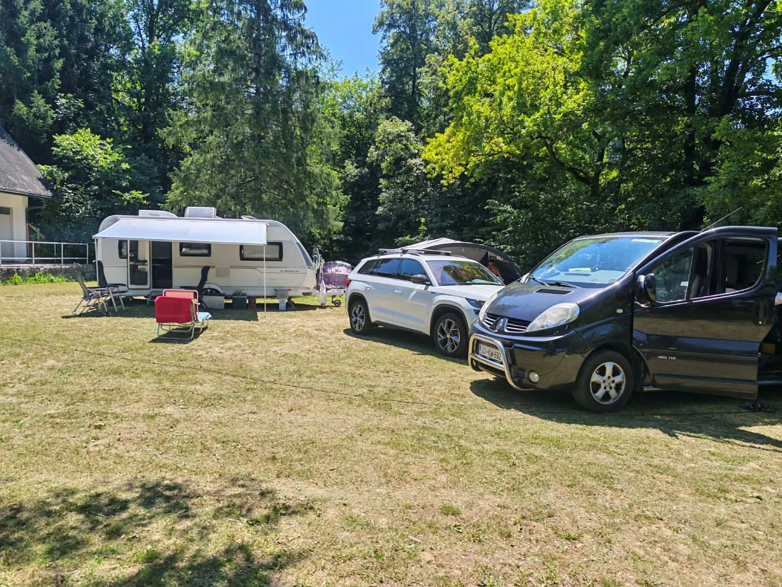 Karavan in avtomobila na travniku, prazen rdeč stol čaka na gosta