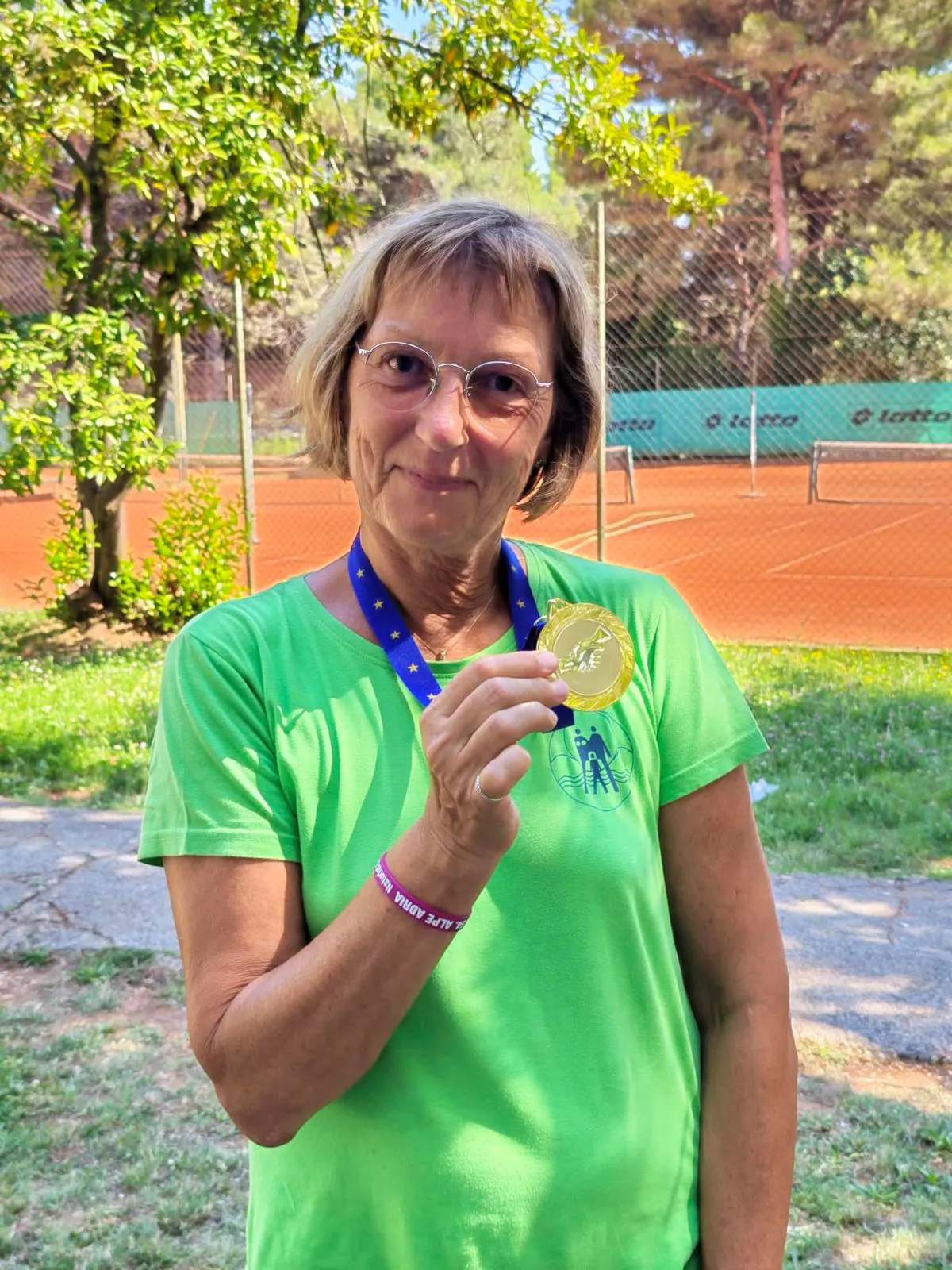 Moški z medaljo in zeleno brisačo čez ramo se nasmehne v kampu
